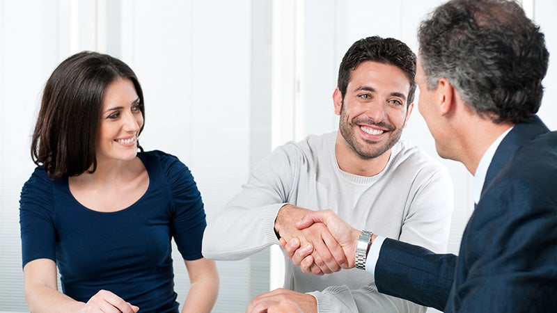 a woman sitting next to a man shaking hands with a car salesman